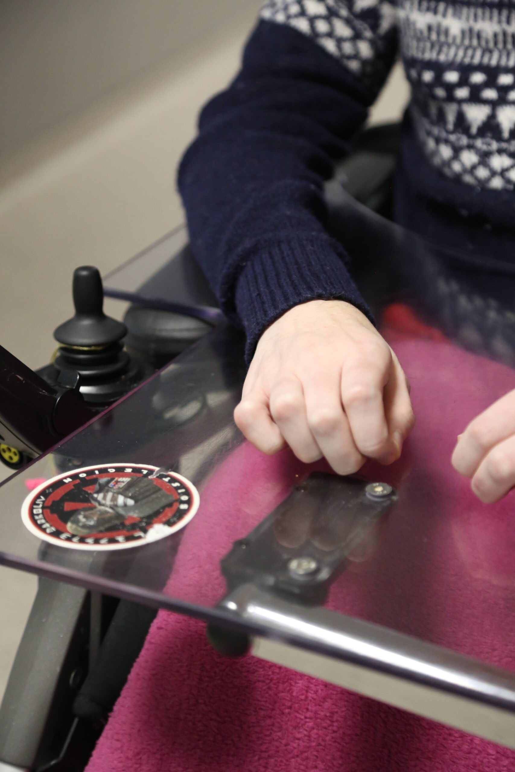 Photo en gros plan de la main d'une personne en situation d'handicap sur un fauteuil roulant motorisé