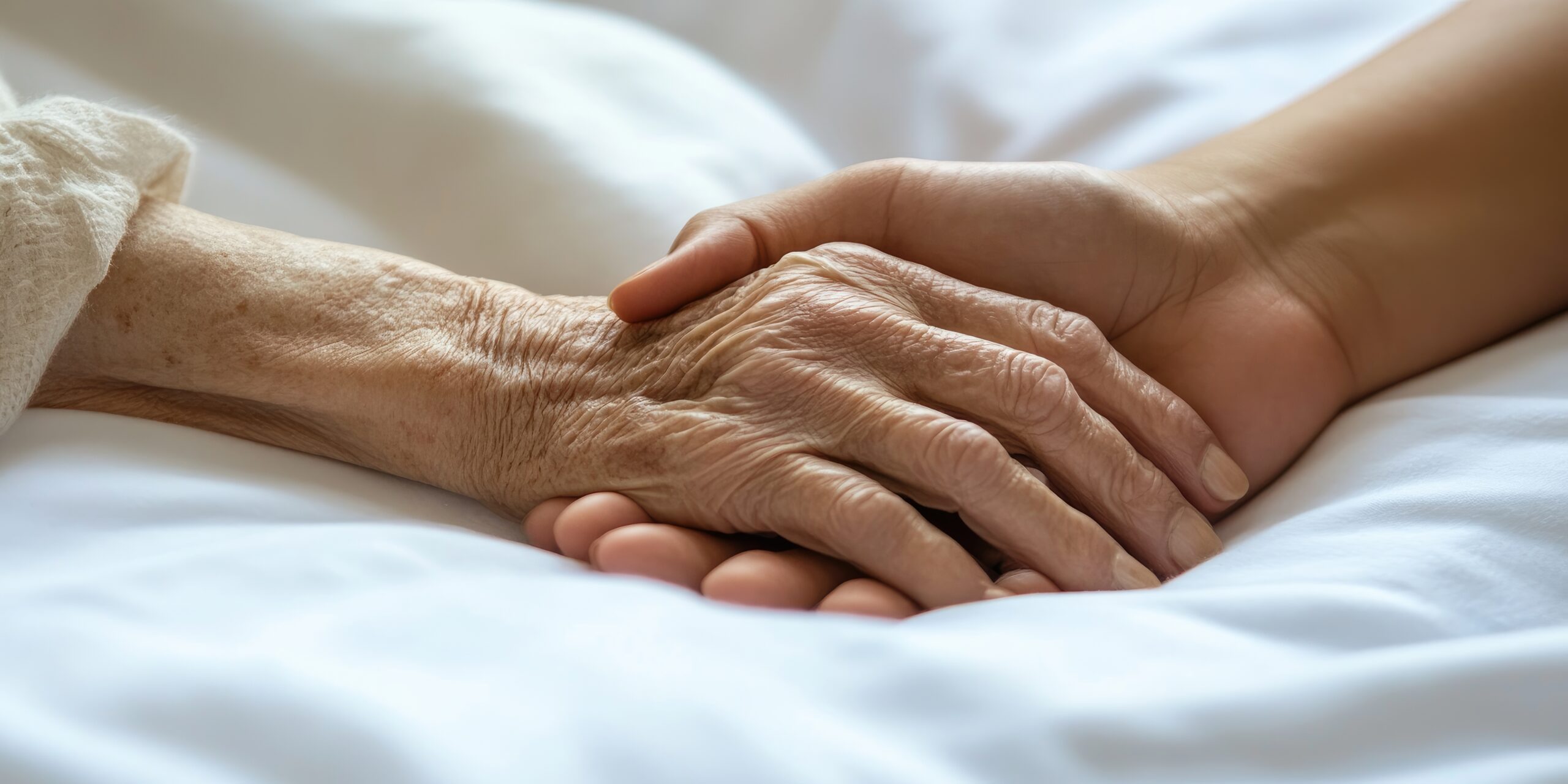 Photo d'une personne tenant la main d'une personne âgée alitée aux soins palliatifs